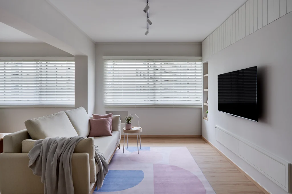 Bright living room with pastel area rug, sofa, and TV wall beside wide windows.