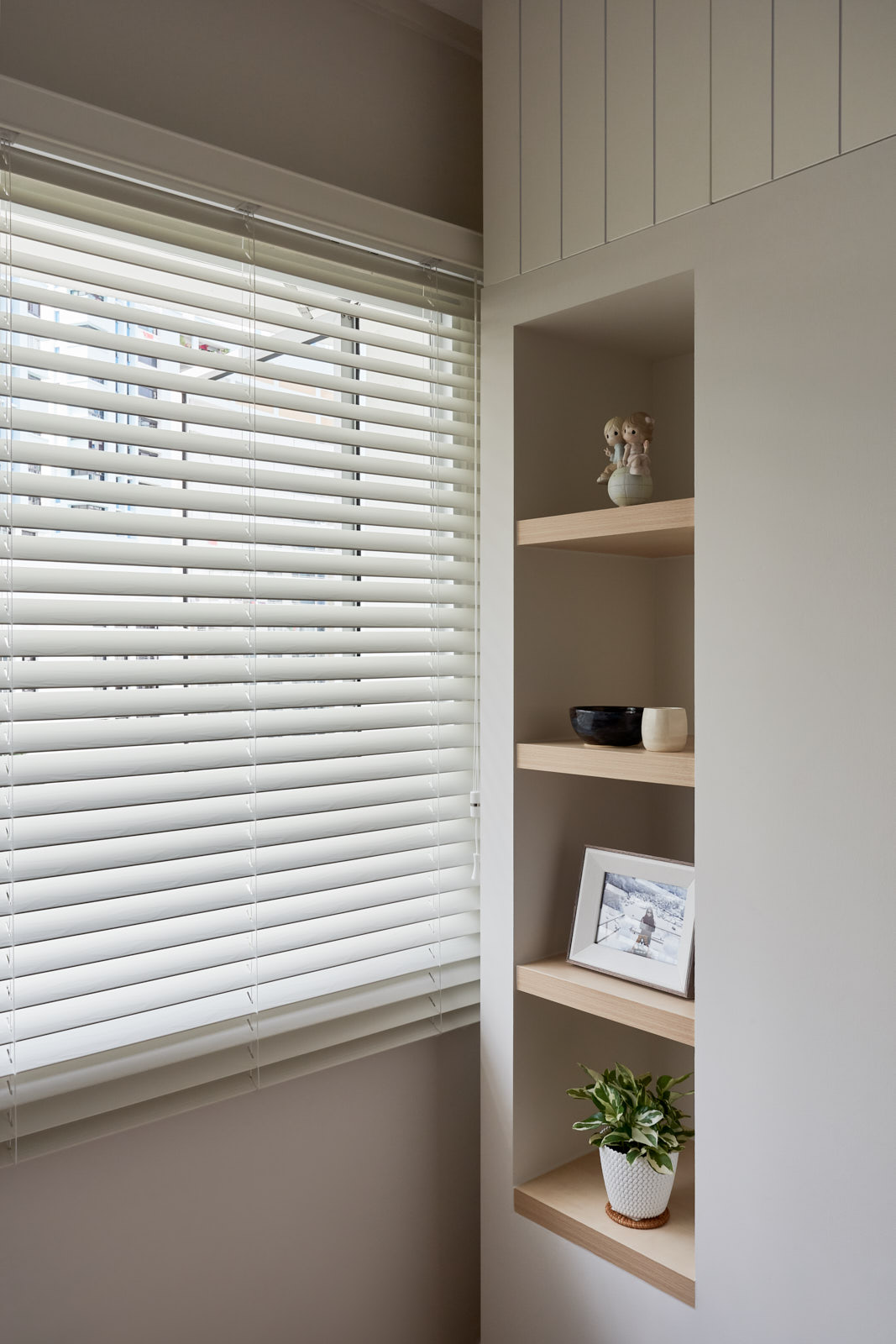 Close-up of window blinds beside built-in shelves with decor.
