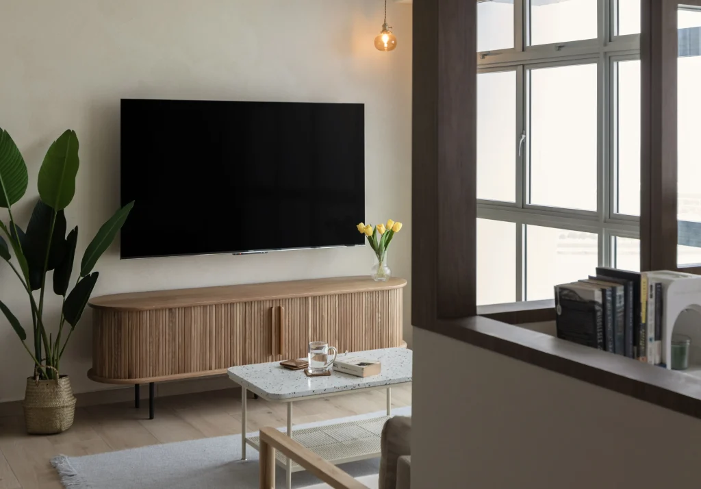Wall-mounted TV above a slatted wood console with a small wall sconce.