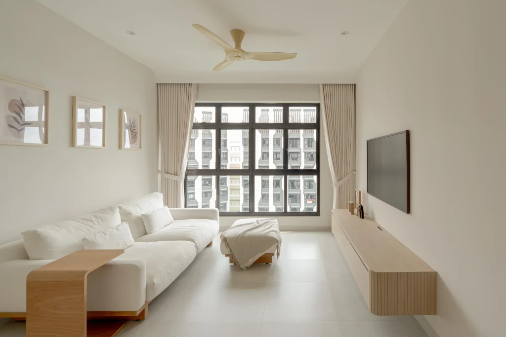 Bright living room with large window, L-shaped sofa, ceiling fan, and wall-mounted TV.