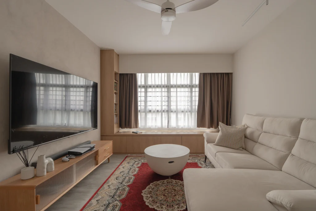 Bright living room with sofa, TV console, patterned rug, large windows, and a ceiling fan.