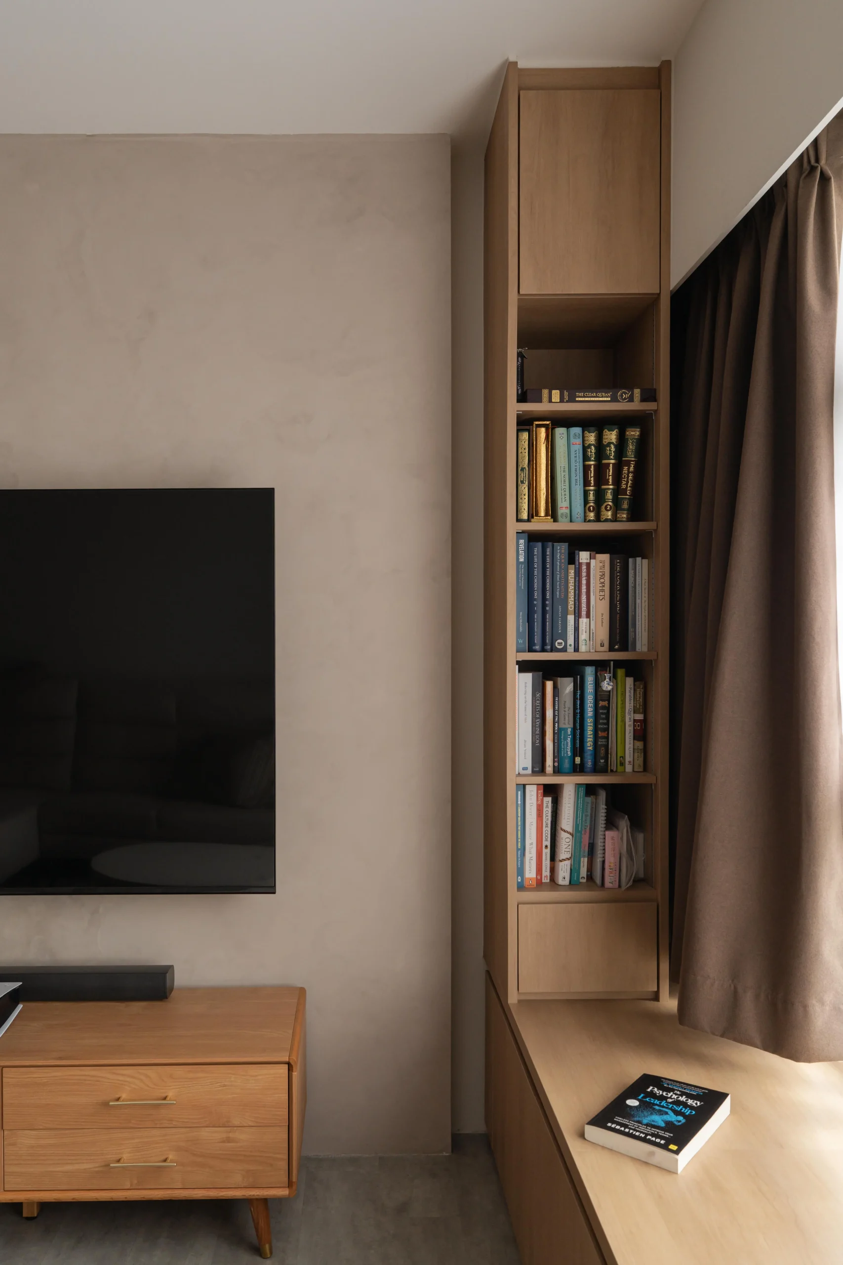 Tall recessed bookshelf next to a wall-mounted TV and curtain