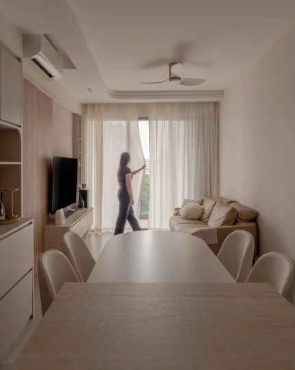 Dining area opening to a bright balcony, with sheer curtains and a person standing at the doorway.