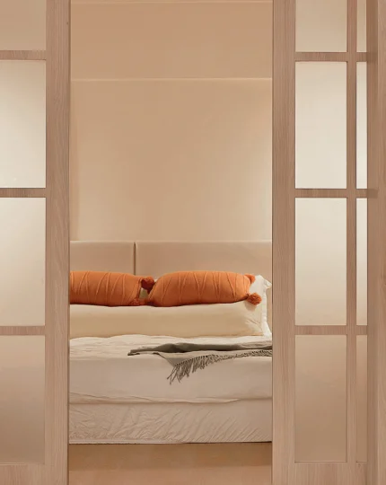 Bed with orange bolster and blanket framed by door panels.