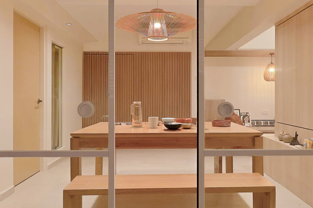 Warm dining room with wooden table, woven pendant, and slatted feature wall seen through glass doors.