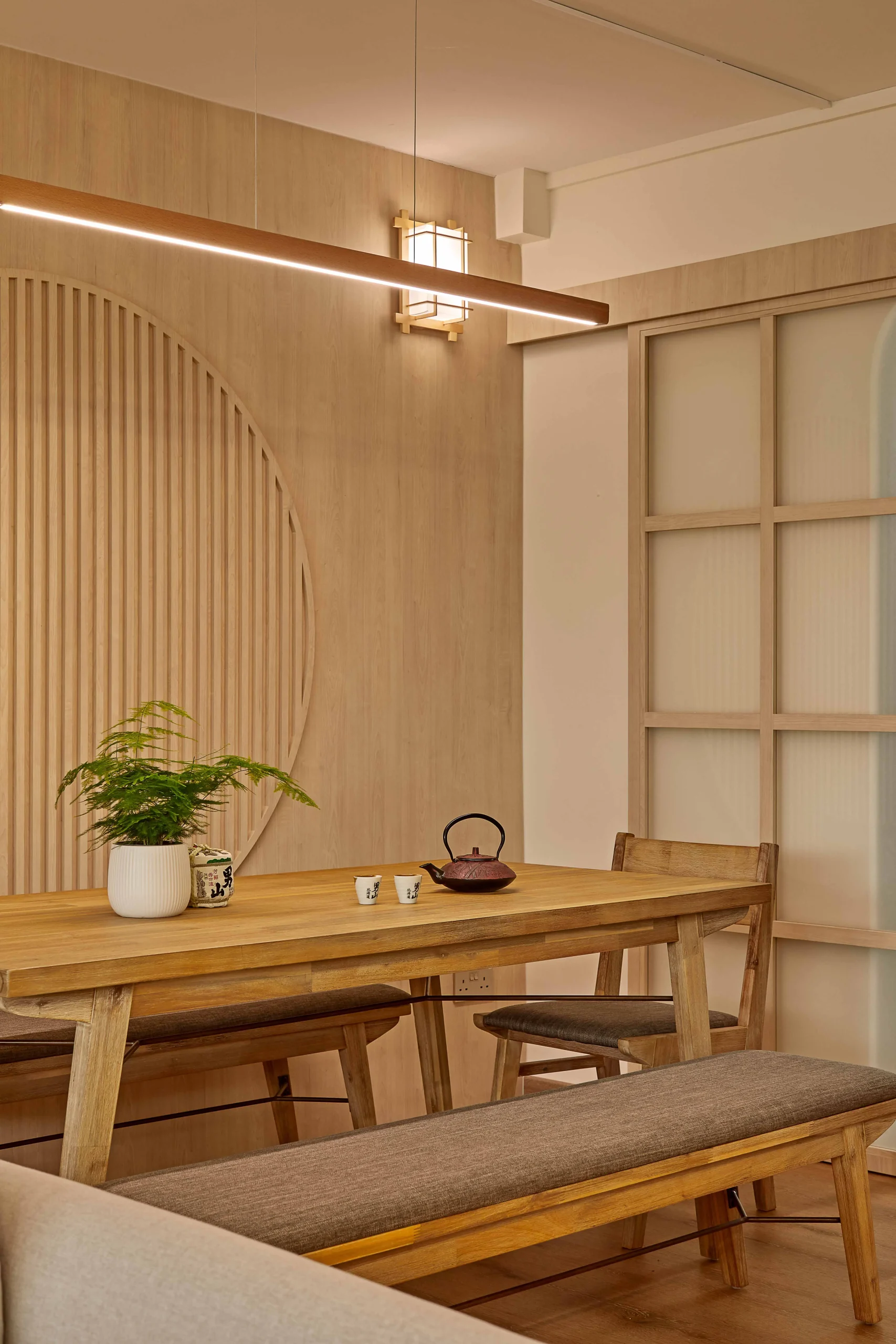 Close-up of wooden dining table under the circular slatted feature with a small potted plant.